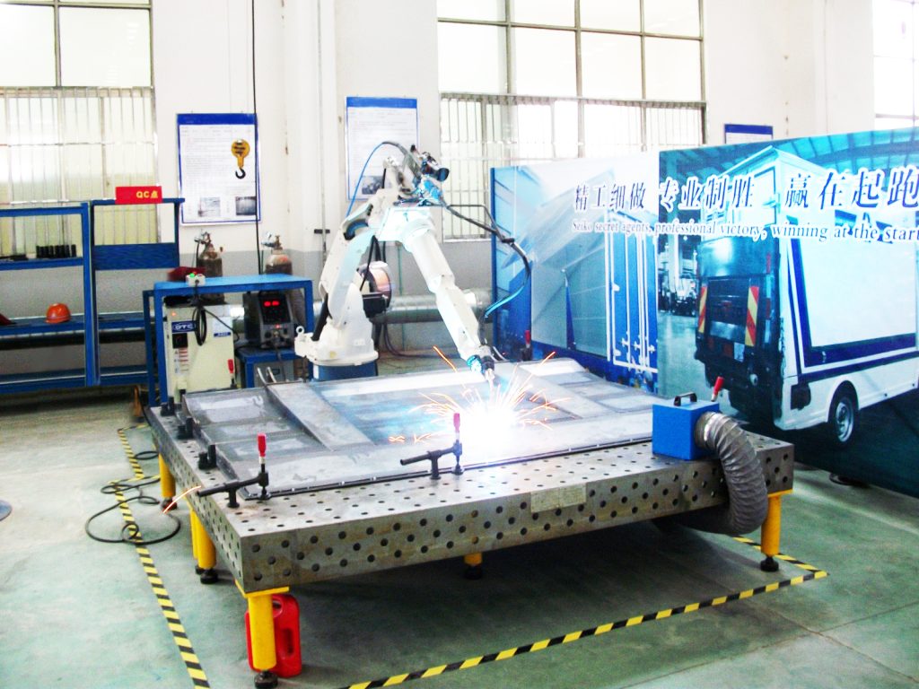 Worker welding tail lift steel frame on a production line inside a certified liftgate manufacturer facility

