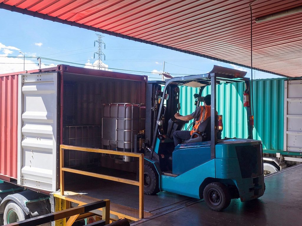 Forklift driving across a dock leveler into a shipping container during loading