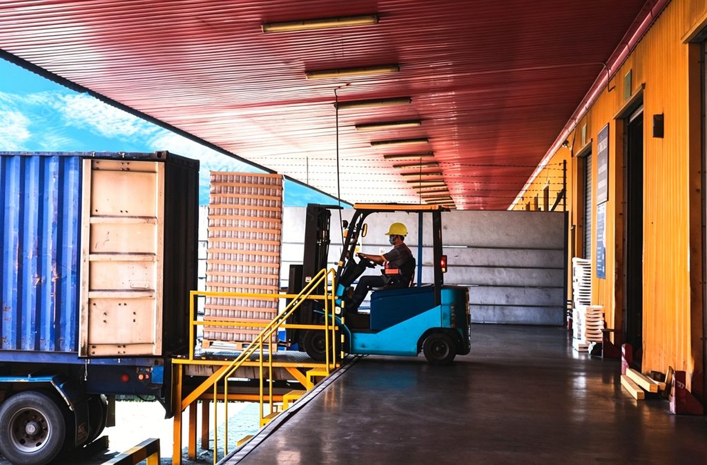 Forklift driving across a dock leveler plate to load a truck, illustrating the repeated impact load the deck plate absorbs