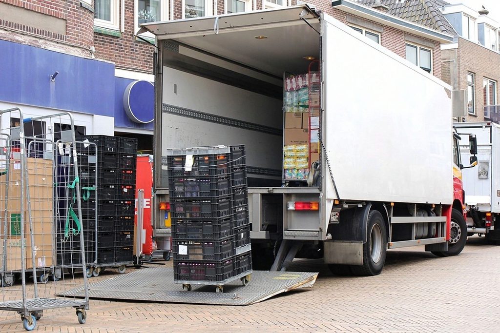 Delivery truck on a brick street with its tail lift lowered to the ground and a wheeled crate stack on the platform