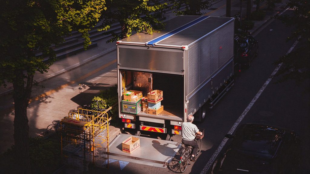 Aerial view of a delivery truck parked roadside using its tail lift to unload cargo during a multi-stop route.