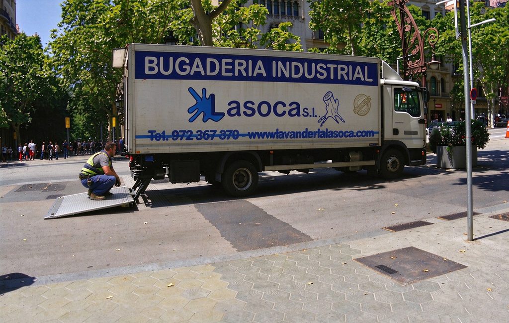 Technician crouching on a truck tail lift platform to inspect the rear of the vehicle