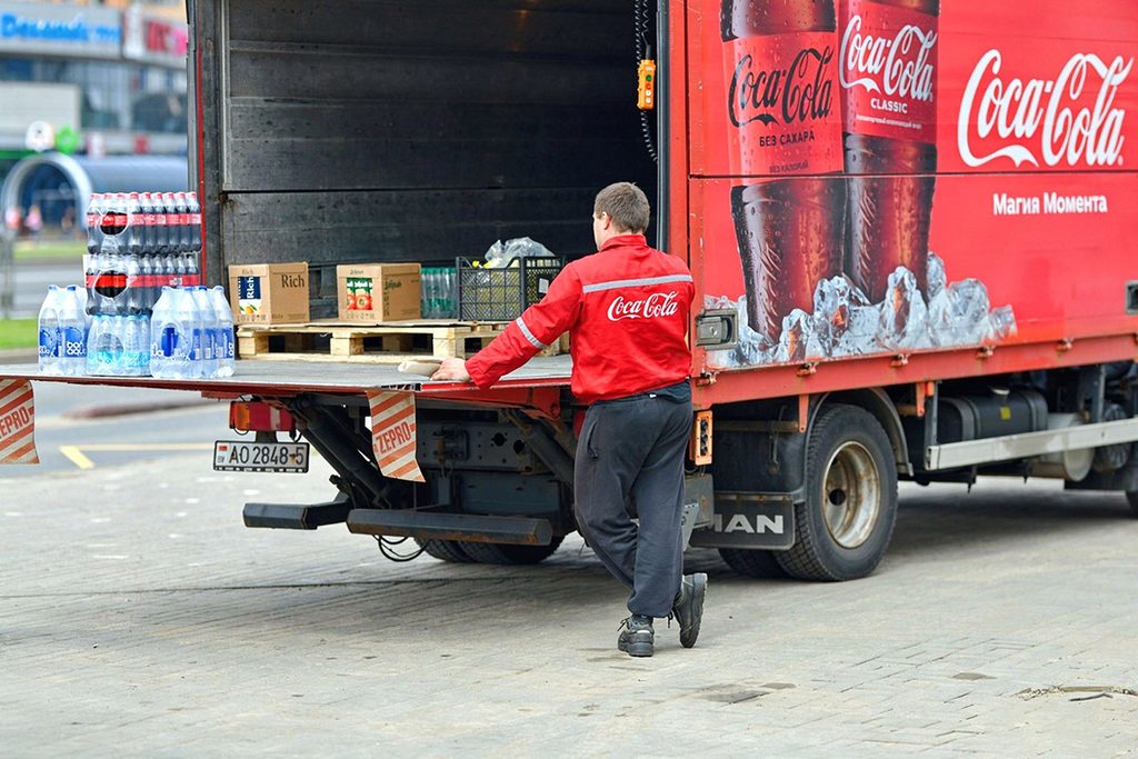 A delivery driver working on an urban distribution truck to optimize truck liftgate weight capacity and route efficiency.
