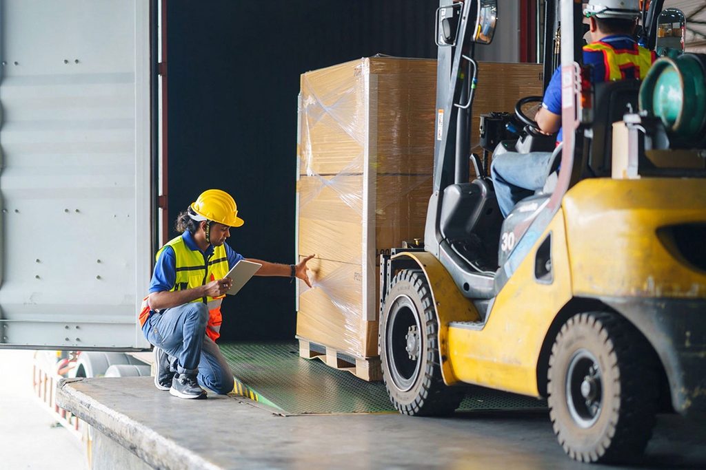 Warehouse worker with tablet inspecting goods during forklift container loading
